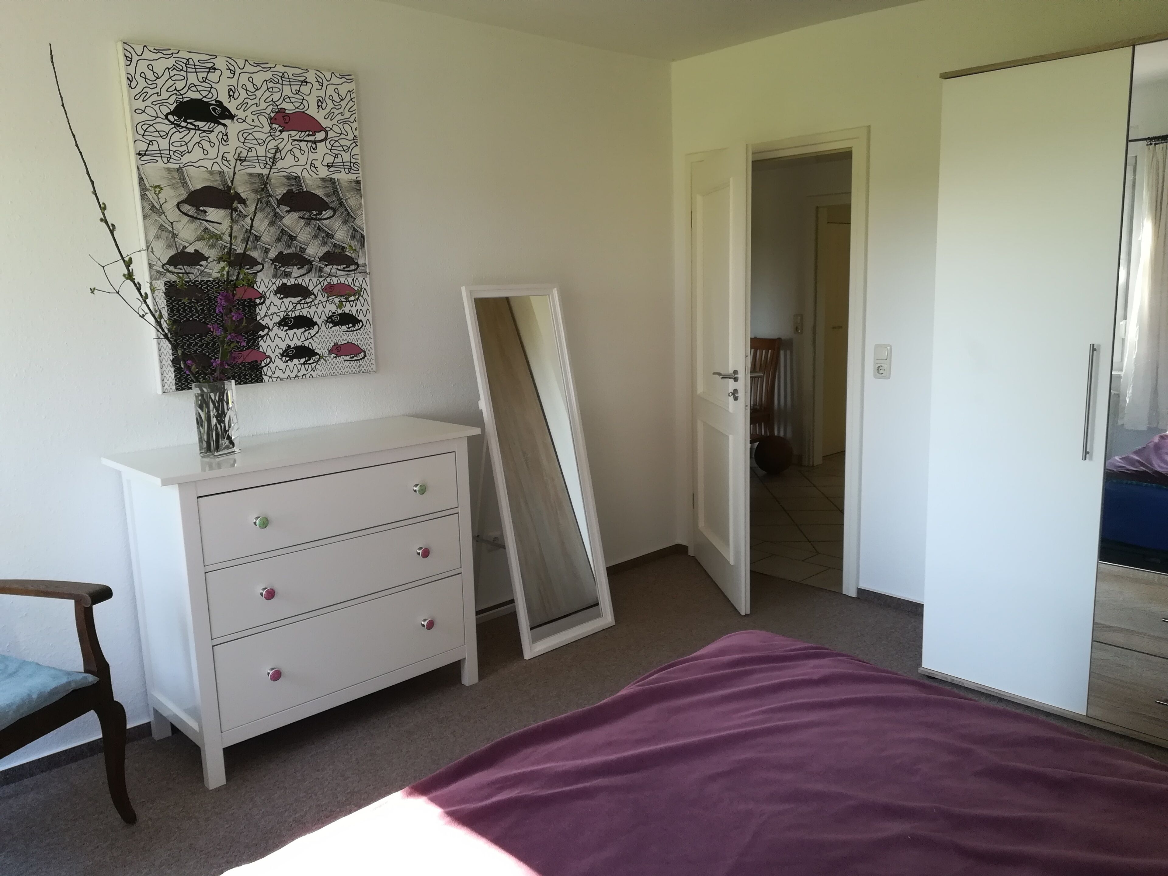 Un dormitorio con cama, cómoda, espejo y puerta que da a otra habitación.