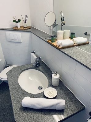 Une salle de bain avec un comptoir en granit, un lavabo blanc, un miroir et des articles de toilette.
