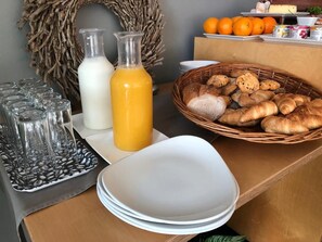 Une table dressée pour le petit-déjeuner avec des verres, une bouteille de lait, une bouteille de jus et un panier de viennoiseries.