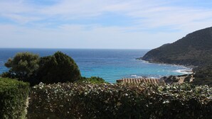 Paisatge costaner amb un viñedo al primer pla i vista al mar i a les muntanyes de fons.
