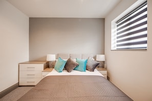 A bedroom with a bed, bedside tables, lamps, and a window with blinds. - 4 Bed - Sleeps 6 - Private Garden - Free Parking (Ashford)
