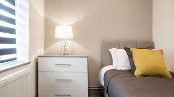 Un dormitorio con cama, mesita de noche, lámpara y ventana con persianas.