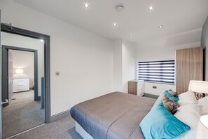 A modern bedroom with a large bed, a bedside table, a mirror, a wardrobe, and a window with blinds. - 4 Bed - Sleeps 6 - Private Garden - Free Parking (Ashford)