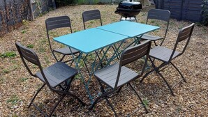 A blue outdoor table with four chairs, surrounded by gravel.