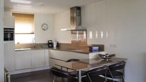A modern kitchen with white cabinets, a stainless steel range hood, a coffee maker, and a clock on the wall. - Porta Isola - Villa Water (Stevensweert)