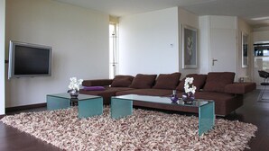 A modern living room with a brown sofa, two glass coffee tables, and a shaggy rug. - Porta Isola - Villa Water (Stevensweert)