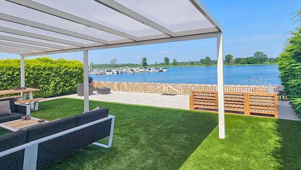 A covered patio with a view of a lake and marina. - Porta Isola - Villa Water (Stevensweert)