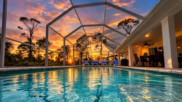 Piscina con vista al atardecer, sillas de descanso y zona de estar cubierta.