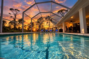A swimming pool with a sunset view, lounge chairs, and a covered seating area.