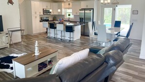 Una cocina moderna con armarios blancos, una isla central con taburetes de bar y una zona de comedor con mesa y sillas.