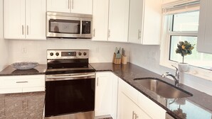 Una cocina con armarios blancos, electrodomésticos de acero inoxidable, encimera de granito y una ventana con una planta.