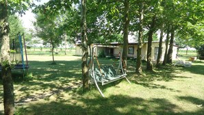 A grassy outdoor area with a swing set, trees, and a building in the background.