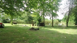 A grassy outdoor area with a swing set, picnic table, and lounge chairs.