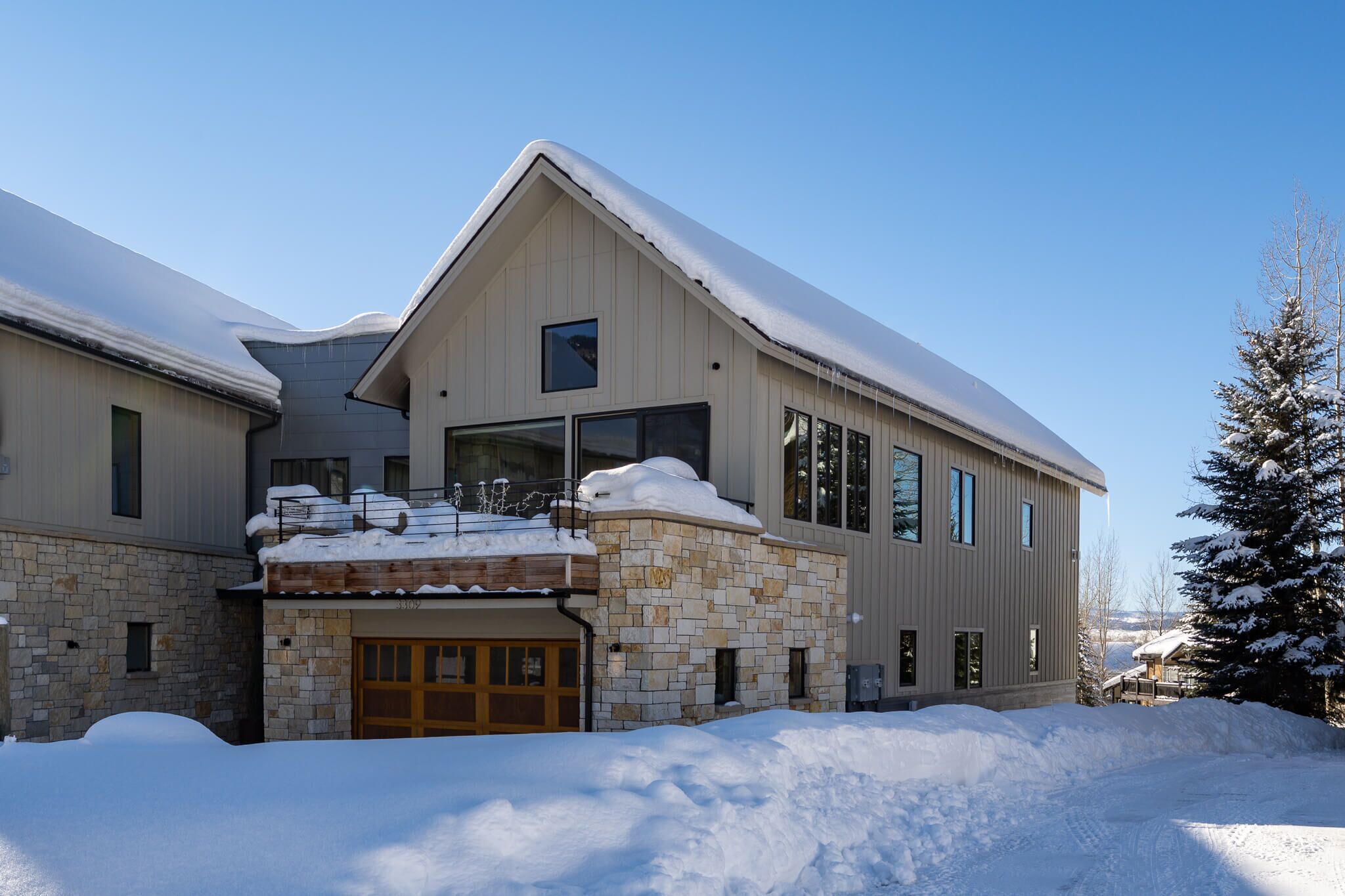 Ein modernes, zweistöckiges Haus mit Steinfundament, großer Garage und schneebedecktem Dach.