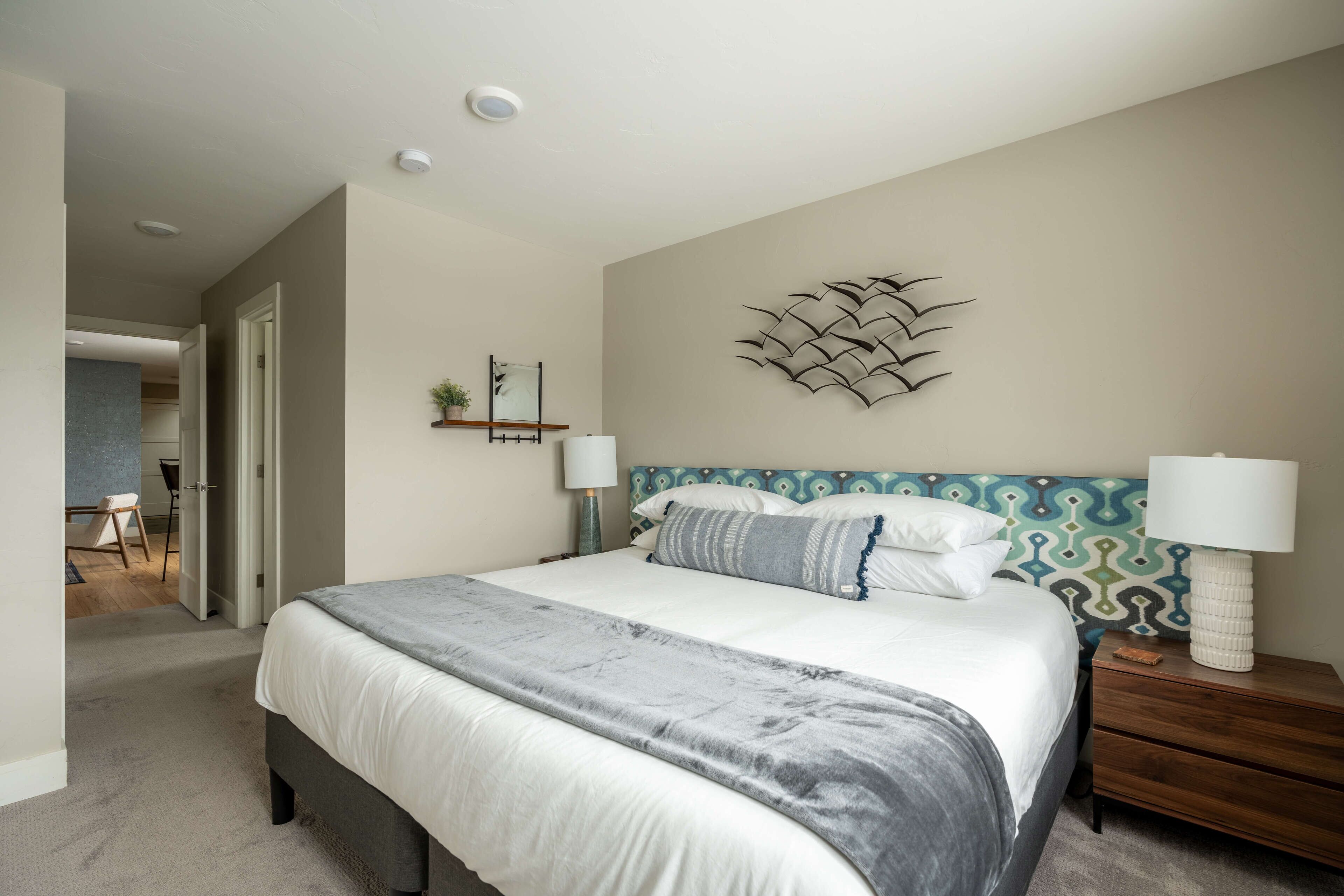 A bedroom with a large bed, bedside tables, a wall-mounted light fixture, and a decorative wall piece.