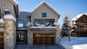 Ein zweigeschossiges Haus mit Garage, Steinwänden und einem mit Schnee bedeckten Dach.