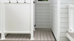 Une maison en bois blanche, avec une clôture blanche, une petite fenêtre et un chemin de pierre menant à l’entrée.