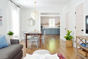A modern living room with a grey sofa, a dining table with chairs, a chandelier, and a kitchen in the background. - Doublemint Townhouse, Walk to Beach & Downtown (Cape Charles)