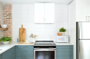 A kitchen with teal cabinets, a microwave, a stove, and a brick wall. - Doublemint Townhouse, Walk to Beach & Downtown (Cape Charles)