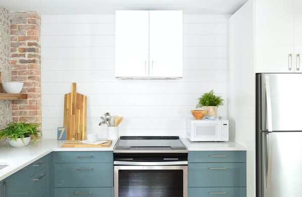 Une cuisine avec des armoires de couleur turquoise, un four à micro-ondes, une cuisinière et un mur en briques.
