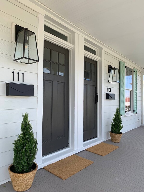 A white wooden house with numbered doors, 111 and 113, and two potted evergreen trees. - Doublemint Townhouse, Walk to Beach & Downtown (Cape Charles)