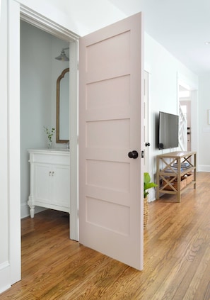 A room with a wooden floor, a white door, a white vanity with a mirror, and a television on a wooden stand. - Doublemint Townhouse, Walk to Beach & Downtown (Cape Charles)