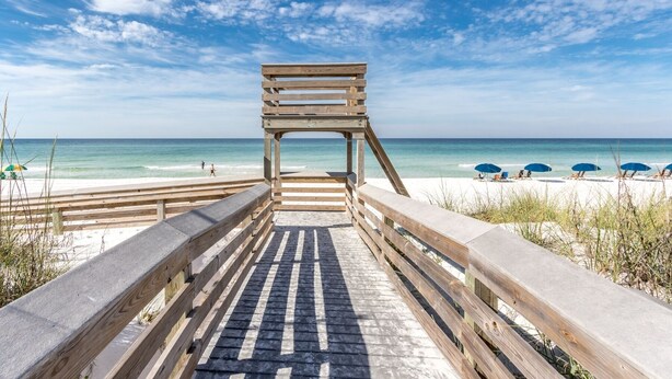 Une promenade en bois menant à une plage agrémentée de parasols et de chaises longues.