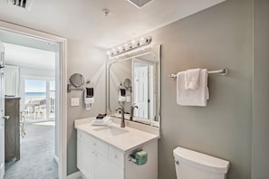 Une salle de bain comprenant un meuble-lavabo, un évier, un miroir avec éclairage, un porte-serviettes et des toilettes.