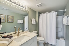Une salle de bain avec un lavabo, un miroir et des toilettes. On y trouve des serviettes et un rideau de douche.