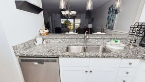 Eine Küche mit Granit Arbeitsplatte, Spüle aus Edelstahl, weißen Schränken und einem Geschirrspüler.