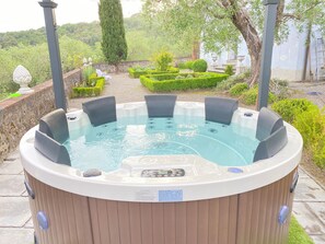 A hot tub with a control panel, surrounded by a garden with neatly trimmed hedges and a stone wall.