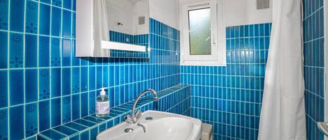Un baño con azulejos azules, un lavamanos blanco, un espejo y una ventana.