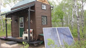 Une petite cabane en bois avec une porte verte, une véranda et des panneaux solaires.