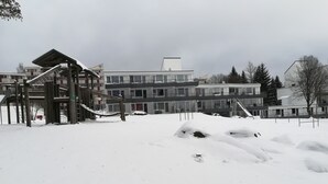 Un espace extérieur enneigé avec une structure en bois, peut-être une terrasse ou un patio, et un immeuble à plusieurs étages en arrière-plan.