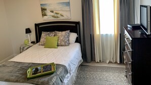 Ein ordentlich eingerichtetes Schlafzimmer mit einem Bett, einem Nachttisch mit Lampe, einem Fernseher und einem Bild an der Wand.