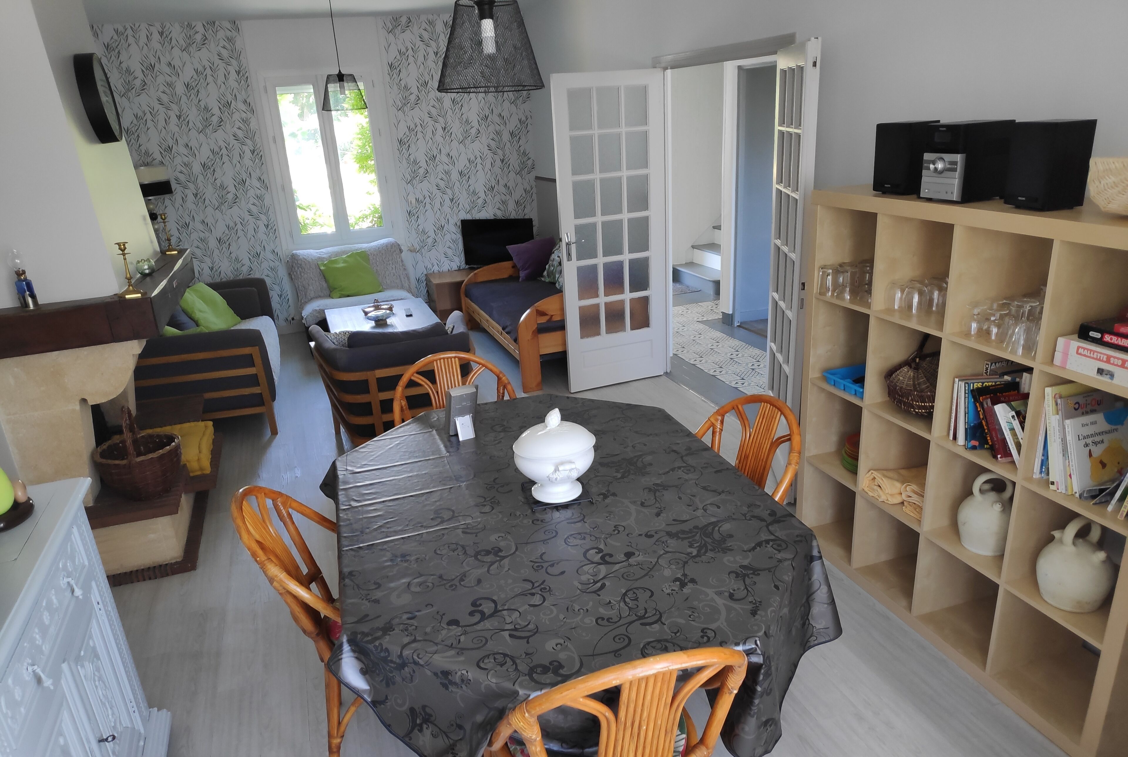 A cozy living area with a sofa, a dining table with chairs, a bookshelf, and a door leading to another room.
