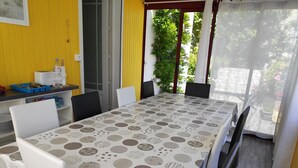 A dining area with a table covered in a patterned tablecloth, surrounded by chairs, and a counter with kitchenware. - Character house for 6 people (Plestin-les-Grèves)