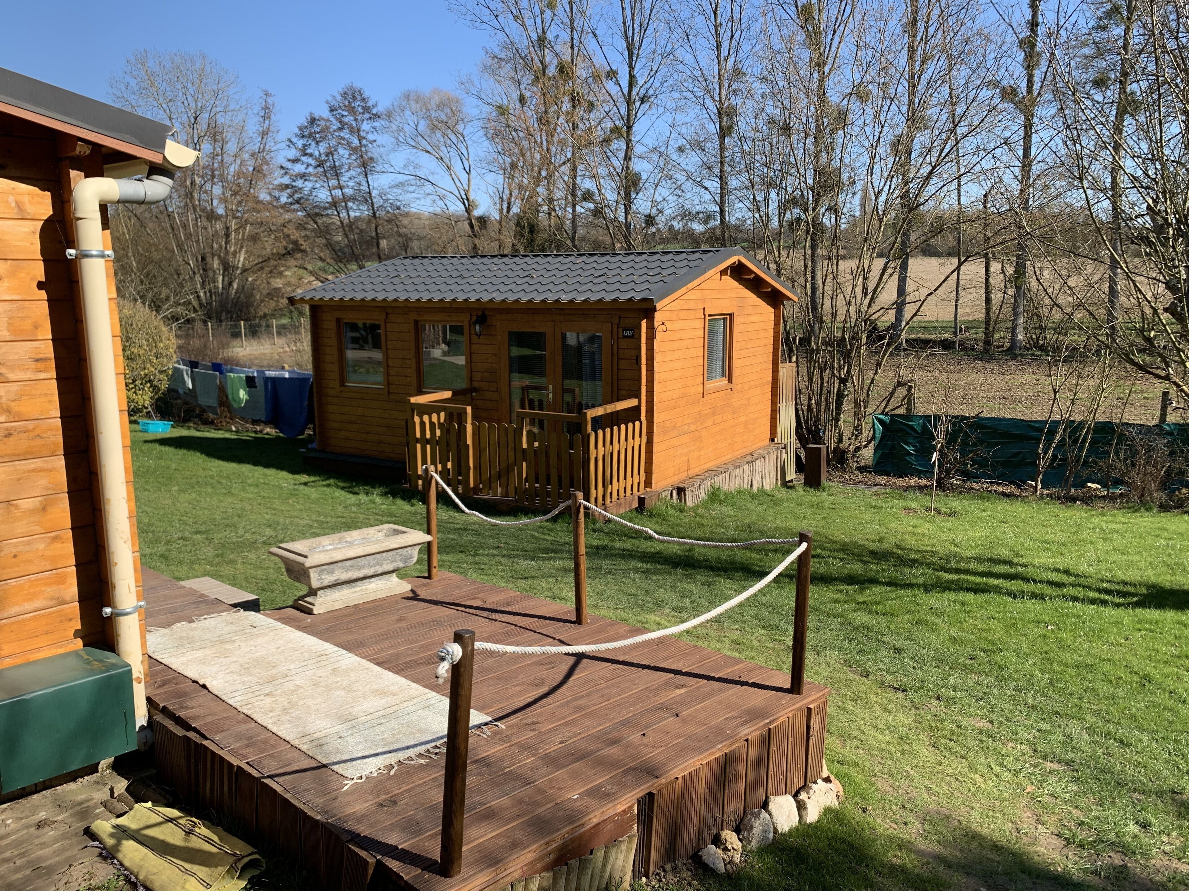A wooden cabin with a fenced deck, a small porch, and a grassy yard.