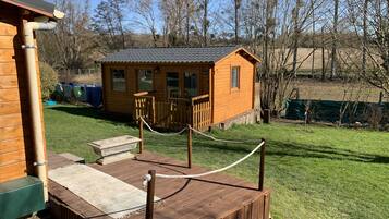 A wooden cabin with a fenced deck, a small porch, and a grassy yard.