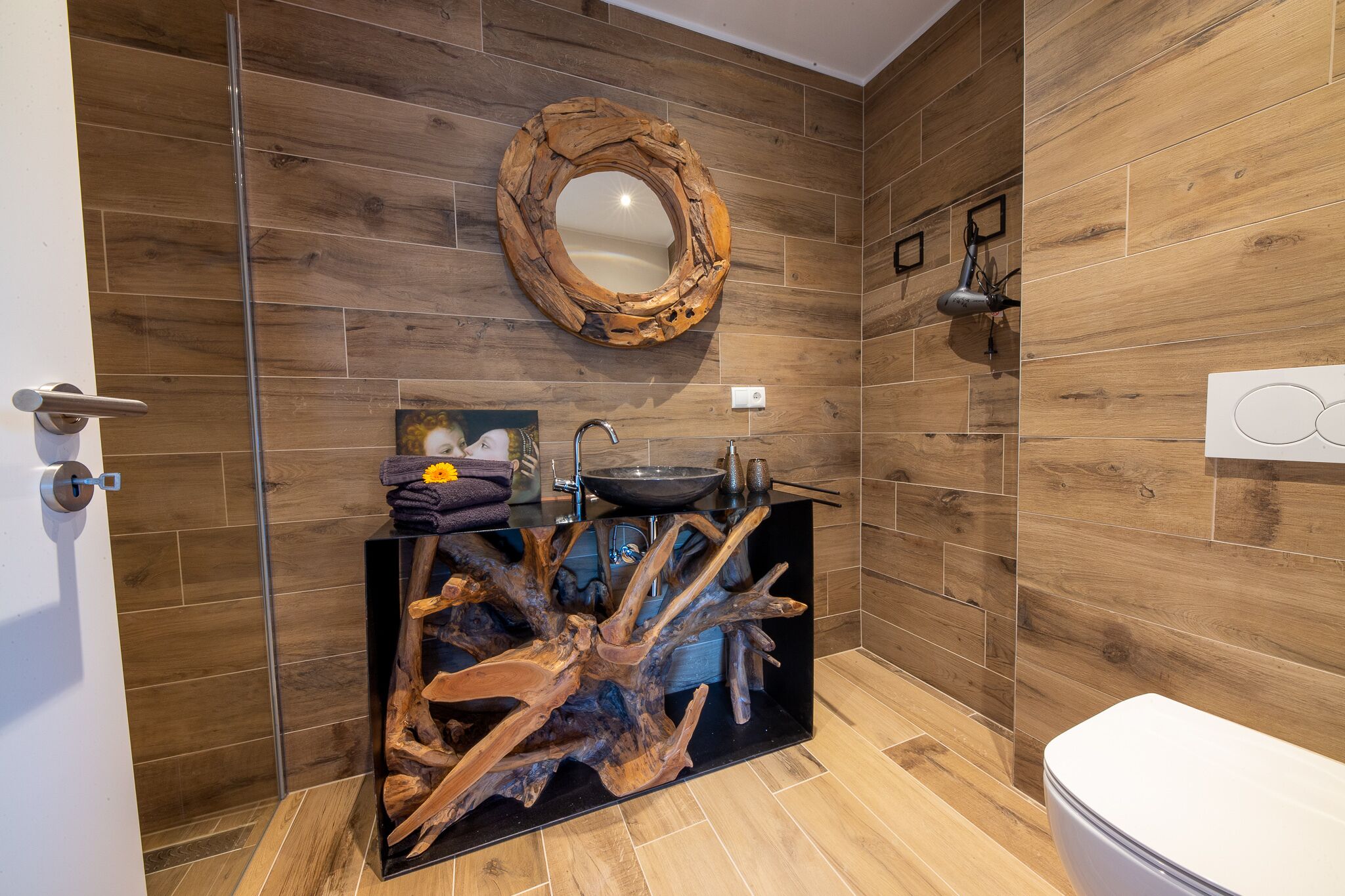 A bathroom with wooden walls, a round mirror, a sink with a wooden base, and a toilet.