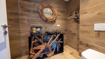 A bathroom with wooden walls, a round mirror, a sink with a wooden base, and a toilet.