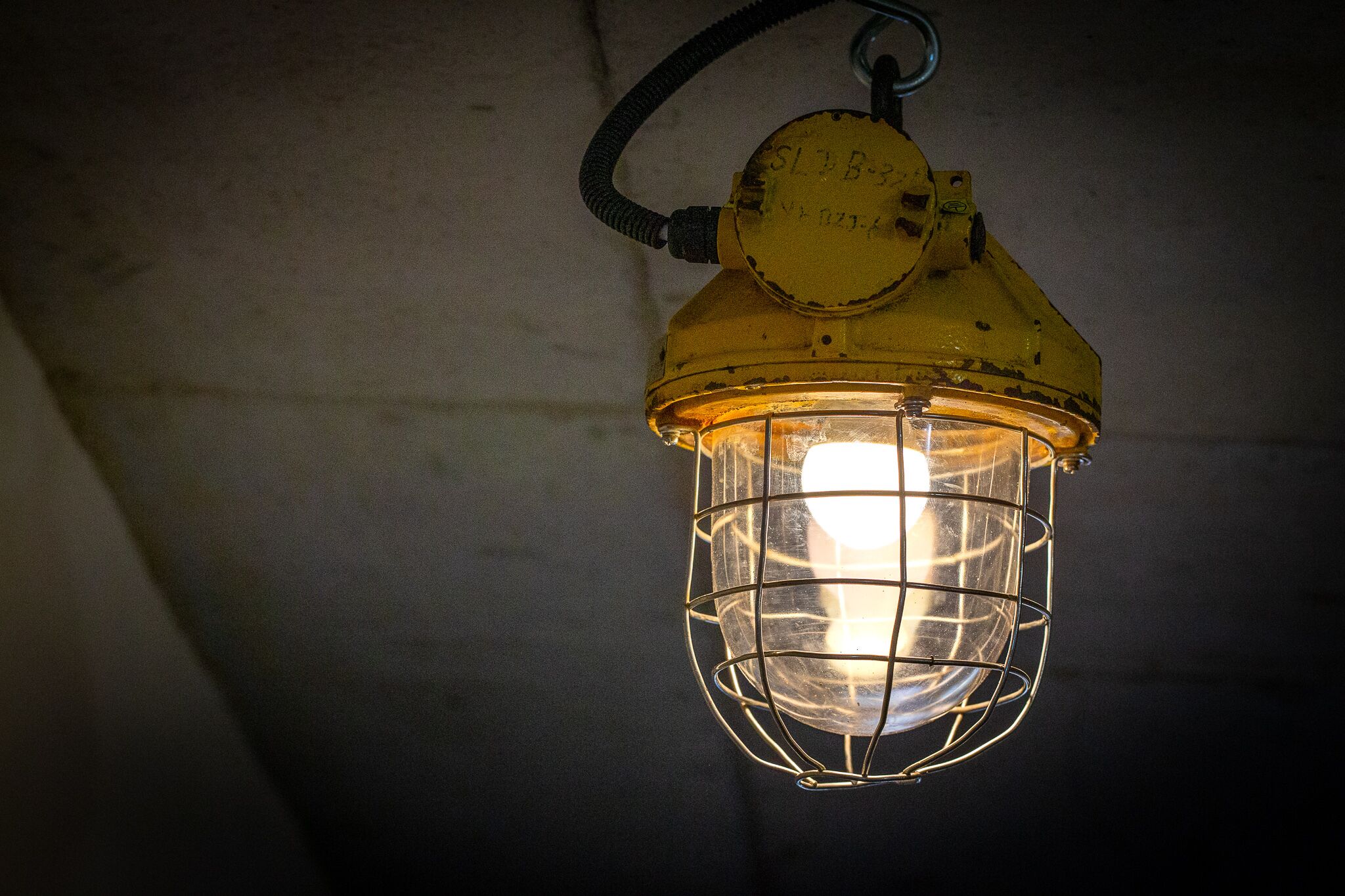 A yellow lantern with a metal wire cage, hanging from a ceiling.