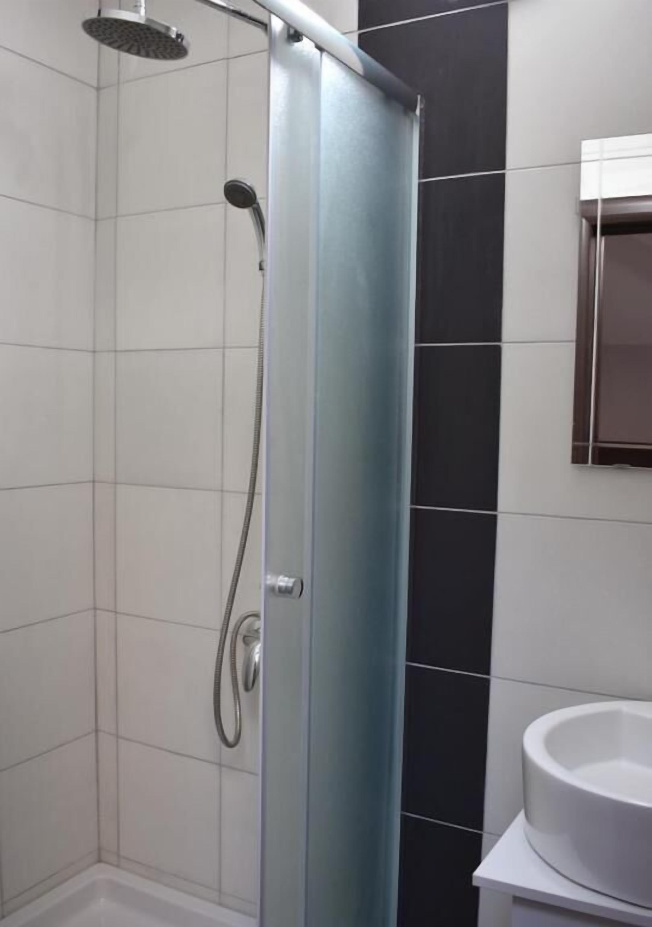 Un bany modern amb plat de dutxa de vidre, un lavabo blanc i una paret revestida de rajoles fosques.