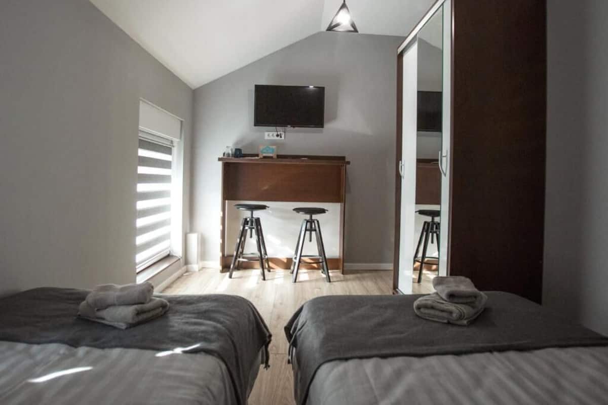 Une chambre avec deux lits, un bureau avec des tabourets, une télévision et une armoire.