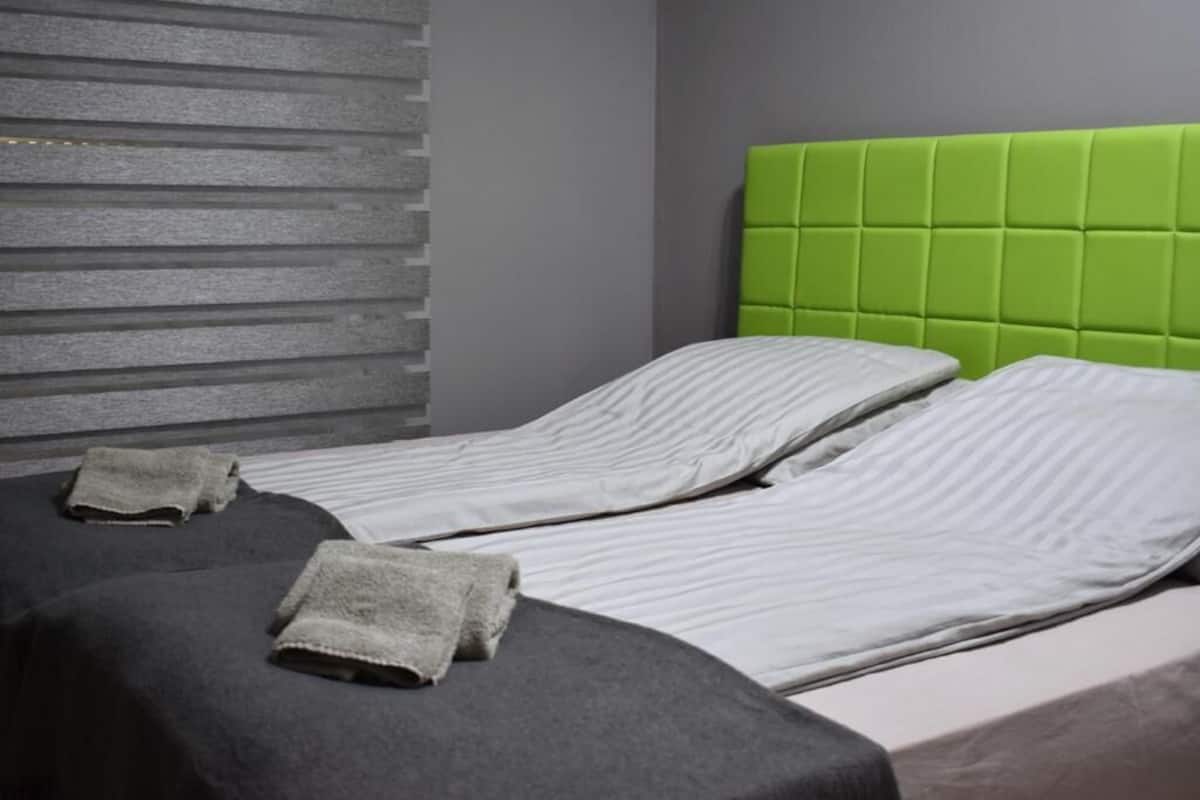 Une chambre avec deux lits, des têtes de lit grises et une tête de lit verte rembourrée.