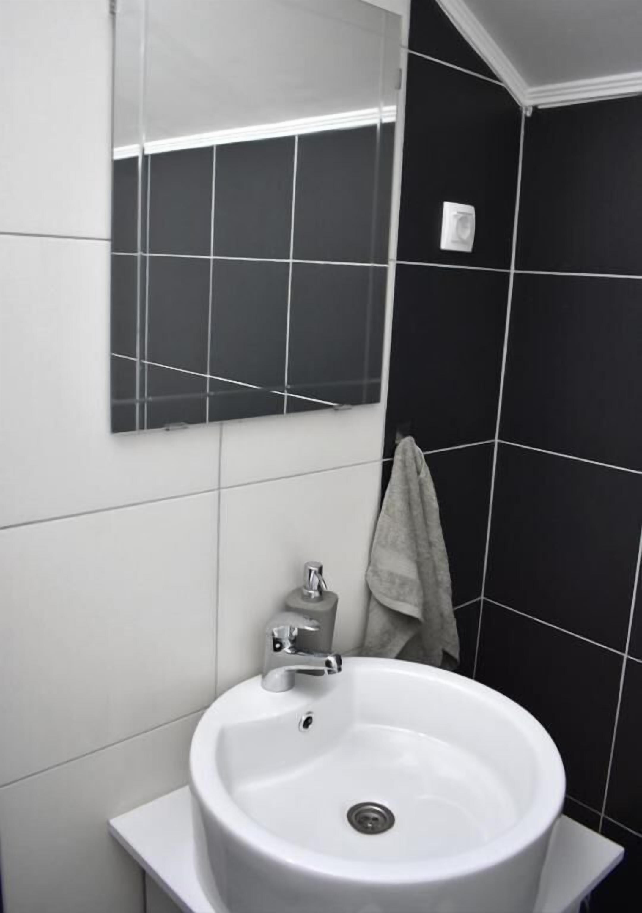Een badkamer met een witte wastafel, een spiegel en zwart betegelde wanden.