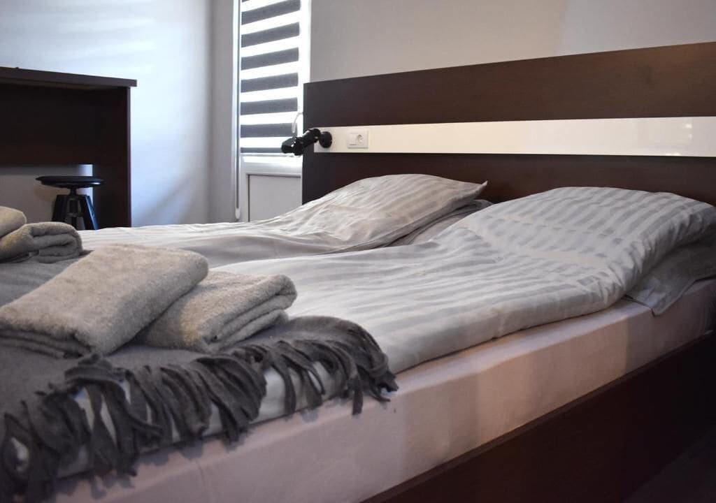 A neatly made bed with a striped bedspread and two pillows, a dark wooden headboard, and a small bedside table with a lamp.