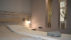 Un dormitorio con una cama grande, una mesita de noche, una lámpara de pared y dos espejos de pared con plantas de orquídea.