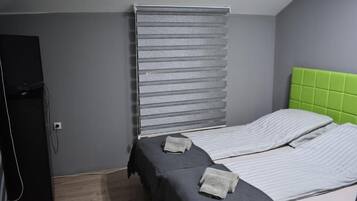 A bedroom with two beds, grey walls, a green headboard, and a window with blinds.