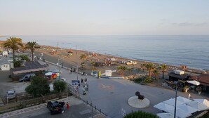 Un paseo marítimo frente a la playa, con vista al mar, palmeras y gente disfrutando.
